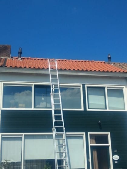 Ladder tegen een woning met rood pannendak voor herstel aan de goot