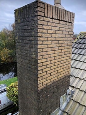 Hoge gemetselde schoorsteen met verweerd voegwerk