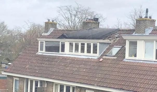 Rij woningen met dakkapellen en beschadigde pannendaken na een storm